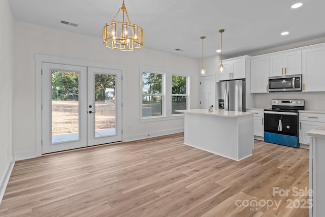 kitchen with appliances with stainless steel finishes, decorative light fixtures, white cabinets, and a center island