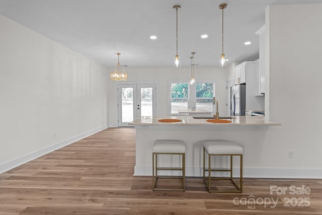 kitchen featuring hanging light fixtures, stainless steel refrigerator, sink, white cabinetry, and a kitchen bar