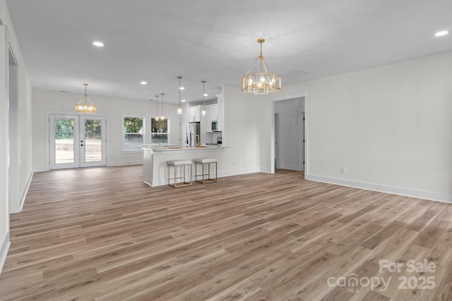 unfurnished living room with an inviting chandelier, french doors, and light hardwood / wood-style flooring