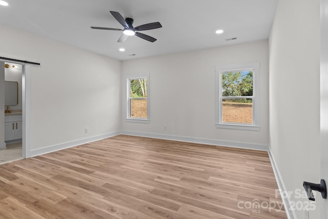 spare room with ceiling fan, a barn door, and light hardwood / wood-style flooring