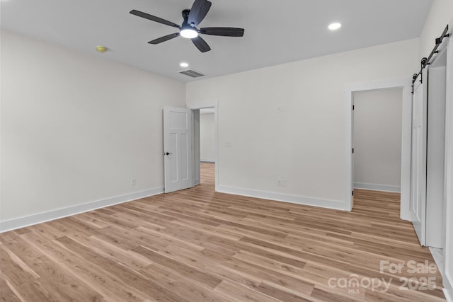 unfurnished bedroom featuring light hardwood / wood-style flooring, ceiling fan, and a barn door