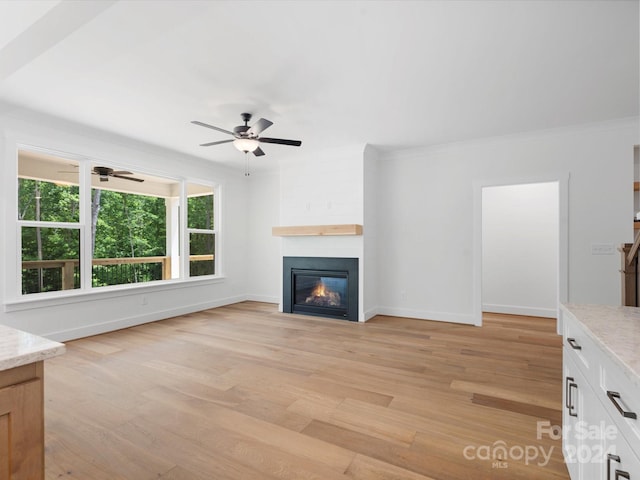 unfurnished living room featuring light wood-type flooring, ceiling fan, crown molding, and a fireplace