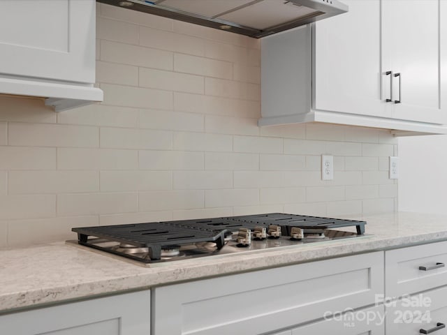 kitchen with backsplash, white cabinetry, wall chimney exhaust hood, and stainless steel gas stovetop