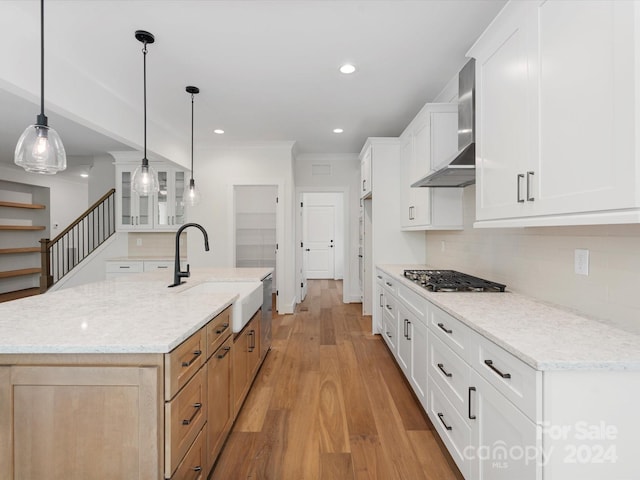 kitchen featuring white cabinets, wall chimney range hood, an island with sink, and light stone counters