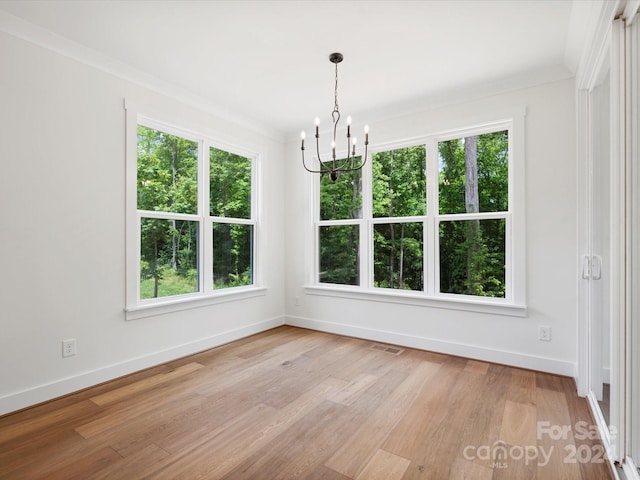 unfurnished dining area with a wealth of natural light, an inviting chandelier, crown molding, and light hardwood / wood-style flooring