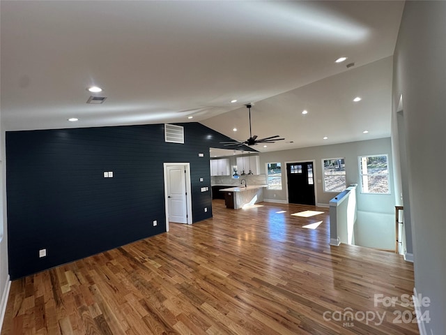 unfurnished living room featuring hardwood / wood-style flooring, vaulted ceiling, ceiling fan, and sink