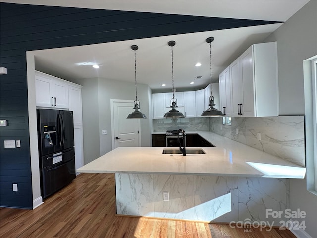 kitchen with white cabinets, black fridge, sink, dark hardwood / wood-style floors, and kitchen peninsula