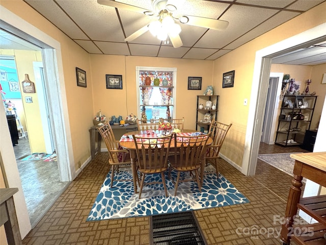 dining space with a drop ceiling and ceiling fan