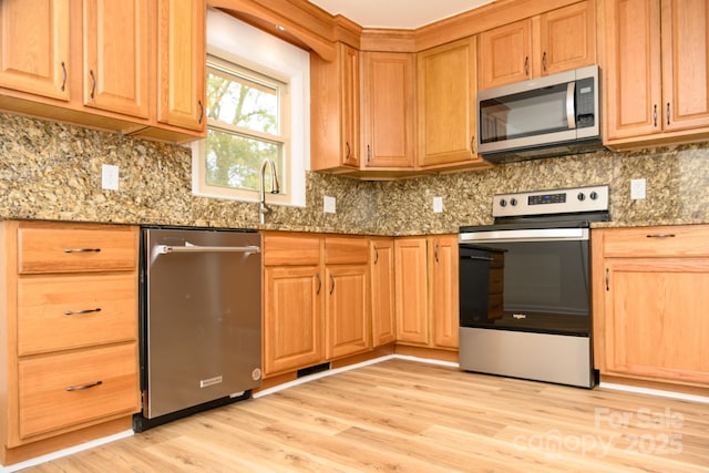 kitchen featuring decorative backsplash, appliances with stainless steel finishes, light hardwood / wood-style flooring, and dark stone countertops