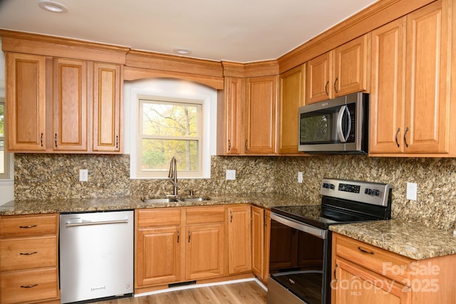 kitchen with appliances with stainless steel finishes, backsplash, dark stone counters, sink, and light hardwood / wood-style floors