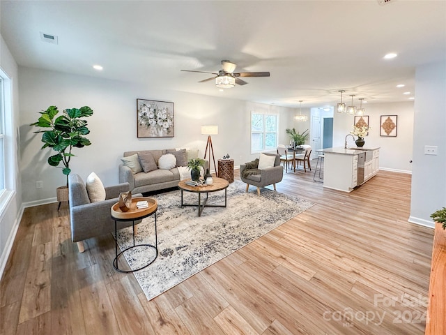 living room with sink, light hardwood / wood-style floors, and ceiling fan with notable chandelier