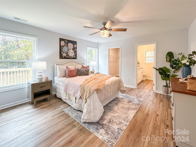 bedroom featuring light hardwood / wood-style floors, multiple windows, ceiling fan, and a walk in closet