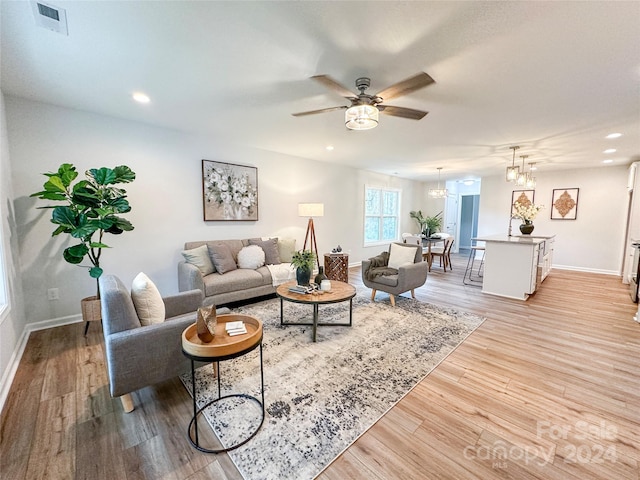 living room featuring light wood-type flooring and ceiling fan with notable chandelier