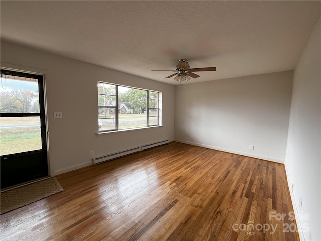 empty room with ceiling fan, a baseboard heating unit, and wood-type flooring