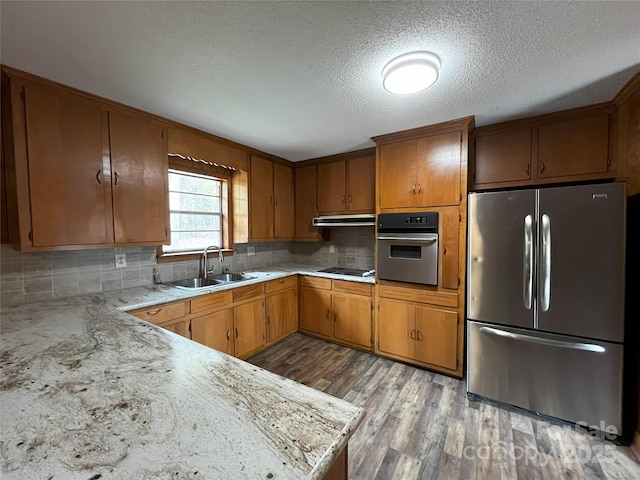 kitchen with light hardwood / wood-style floors, decorative backsplash, sink, stainless steel appliances, and a textured ceiling