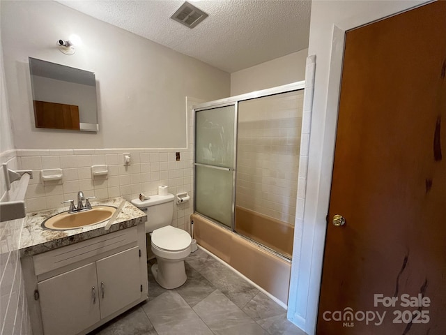 full bathroom featuring toilet, enclosed tub / shower combo, tile walls, a textured ceiling, and vanity