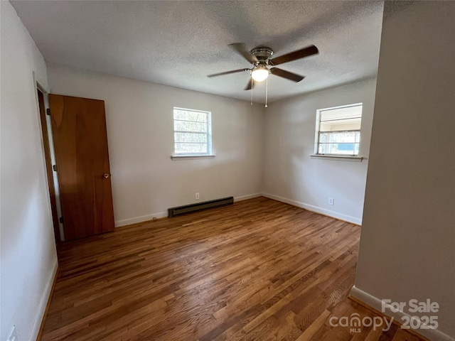 empty room with ceiling fan, a baseboard radiator, hardwood / wood-style floors, and a textured ceiling