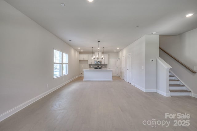 unfurnished living room featuring an inviting chandelier and light hardwood / wood-style flooring