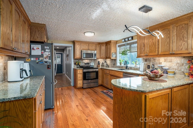 kitchen with light stone counters, stainless steel appliances, sink, light hardwood / wood-style floors, and kitchen peninsula