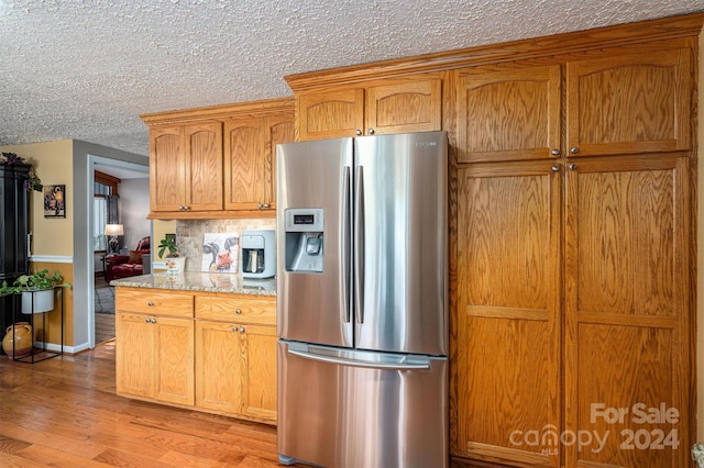 kitchen featuring stainless steel refrigerator with ice dispenser, a textured ceiling, light stone counters, and light hardwood / wood-style flooring