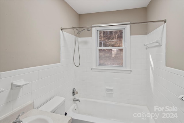 full bathroom featuring vanity, toilet, tiled shower / bath, and tile walls