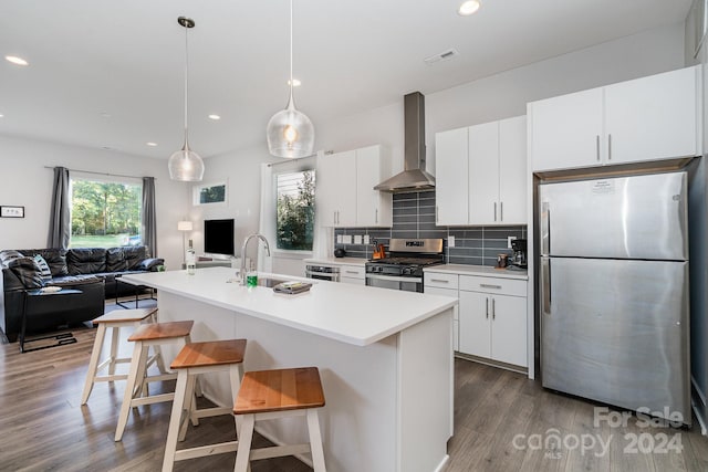 kitchen with stainless steel appliances, sink, wall chimney exhaust hood, a breakfast bar area, and light hardwood / wood-style flooring