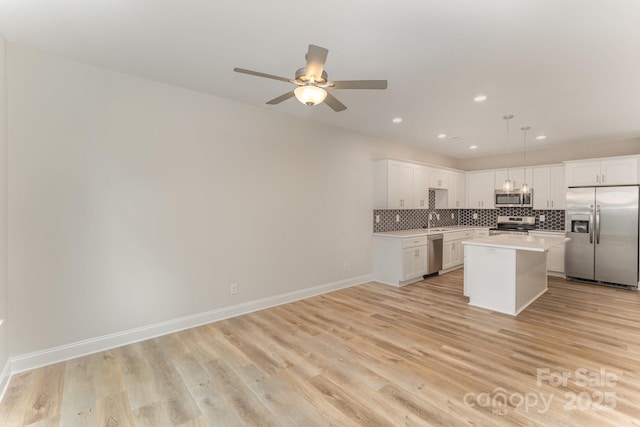 kitchen with a center island, pendant lighting, stainless steel appliances, light countertops, and white cabinets