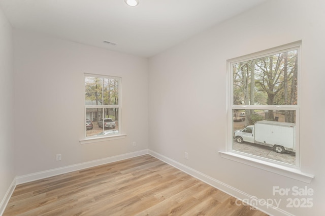 empty room with light wood-style floors, visible vents, and baseboards