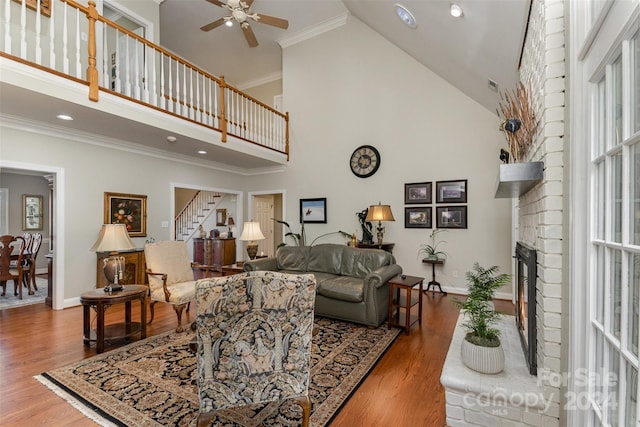 living room featuring hardwood / wood-style floors, ornamental molding, a fireplace, and high vaulted ceiling