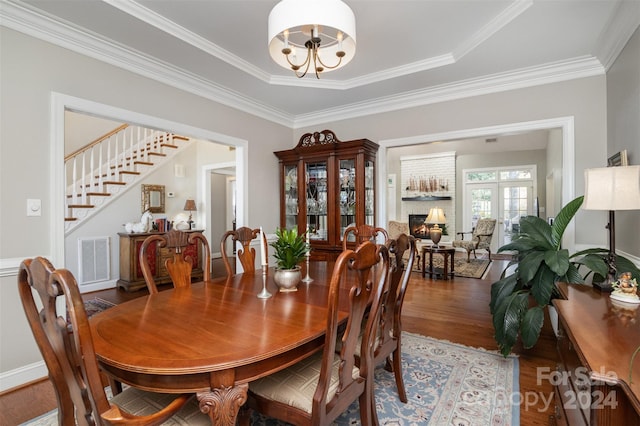 dining area featuring a brick fireplace, ornamental molding, a tray ceiling, hardwood / wood-style flooring, and a chandelier