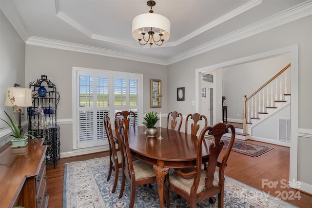 dining area with hardwood / wood-style flooring, a notable chandelier, ornamental molding, and a tray ceiling