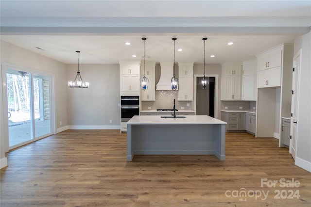 kitchen featuring an island with sink, pendant lighting, light hardwood / wood-style floors, decorative backsplash, and white cabinets