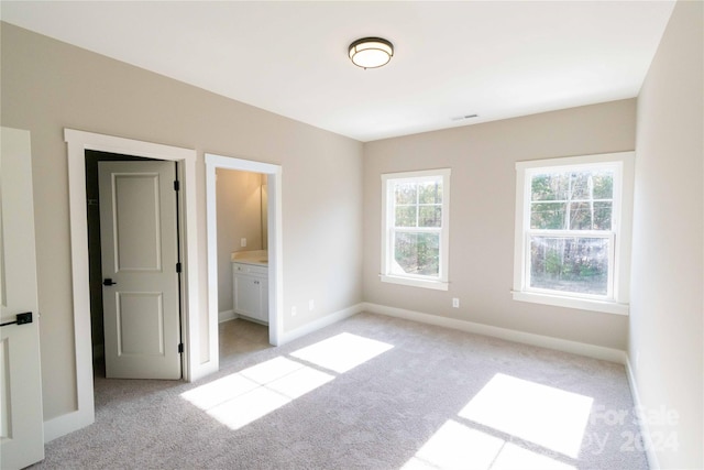 unfurnished bedroom with ensuite bathroom and light colored carpet