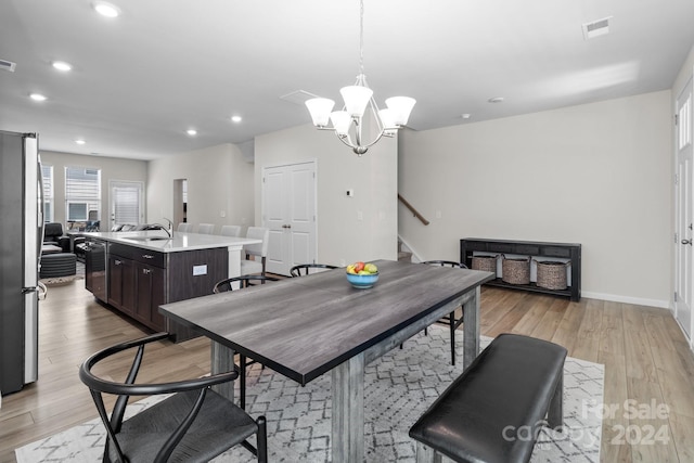 dining space featuring sink, light wood-type flooring, and an inviting chandelier