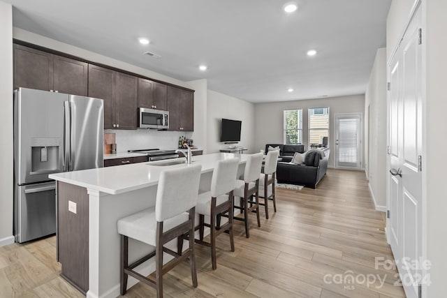 kitchen featuring a kitchen island with sink, light wood-type flooring, appliances with stainless steel finishes, and a kitchen breakfast bar