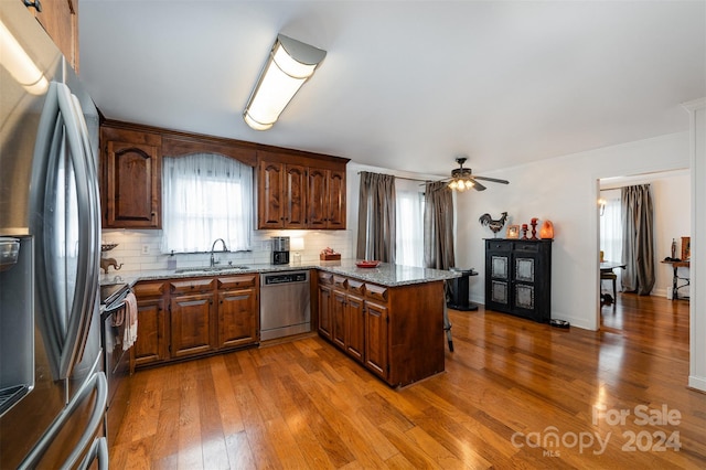 kitchen with wood-type flooring, light stone counters, stainless steel appliances, sink, and kitchen peninsula