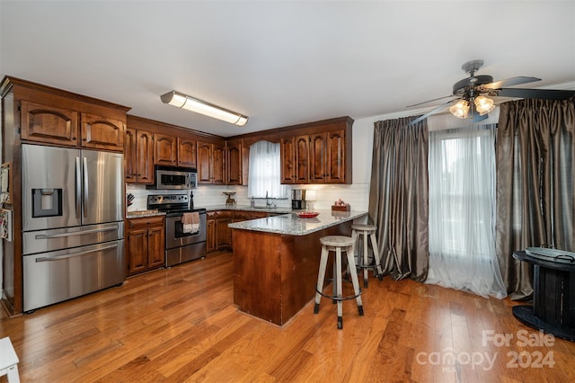 kitchen with stainless steel appliances, kitchen peninsula, a kitchen breakfast bar, backsplash, and light wood-type flooring