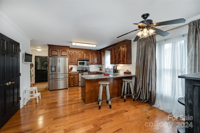 kitchen featuring light wood-type flooring, kitchen peninsula, backsplash, and stainless steel appliances