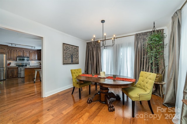 dining area with light hardwood / wood-style floors, an inviting chandelier, and ornamental molding