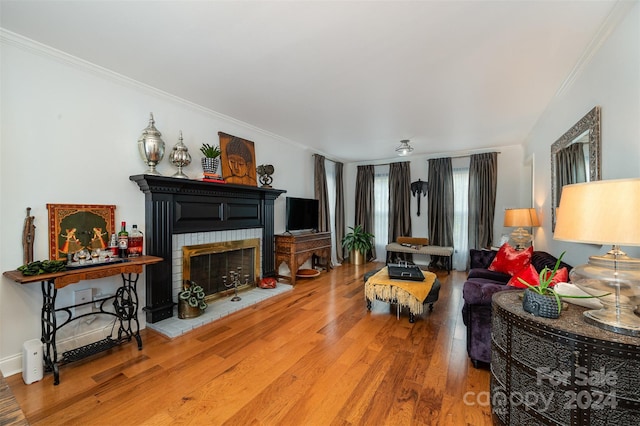 living room with a brick fireplace, wood-type flooring, and crown molding