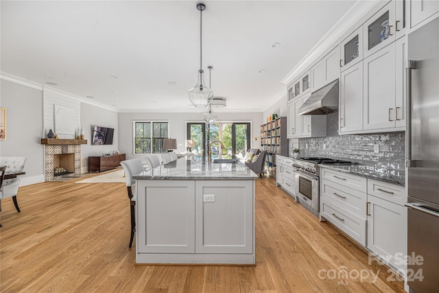 kitchen featuring hanging light fixtures, white cabinets, light wood-type flooring, and ventilation hood