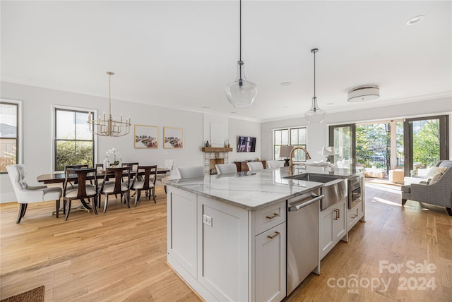 kitchen with dishwasher, an island with sink, hanging light fixtures, and light hardwood / wood-style flooring