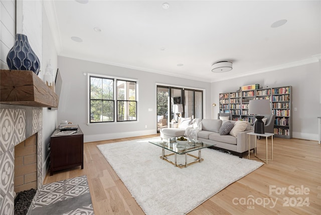 living room featuring a tile fireplace, ornamental molding, and light wood-type flooring