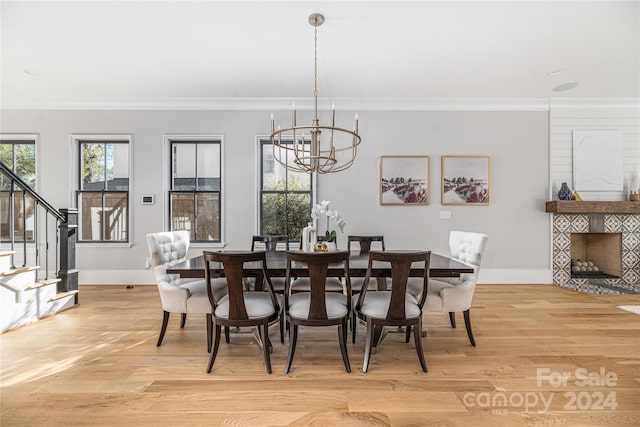 dining space with a tile fireplace, crown molding, a chandelier, and light wood-type flooring