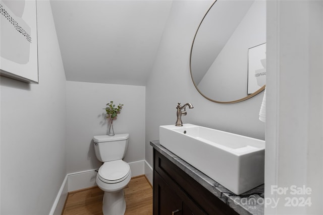 bathroom with toilet, wood-type flooring, vanity, and vaulted ceiling