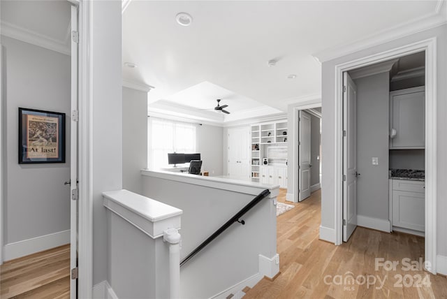 hall featuring a raised ceiling, light wood-type flooring, and crown molding