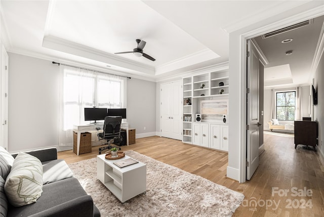 living room with ceiling fan, ornamental molding, light hardwood / wood-style flooring, and a tray ceiling