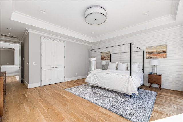 bedroom with a raised ceiling, crown molding, wood walls, and light wood-type flooring