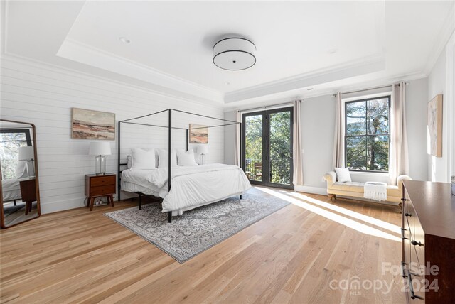 bedroom featuring a raised ceiling, light hardwood / wood-style flooring, and wooden walls