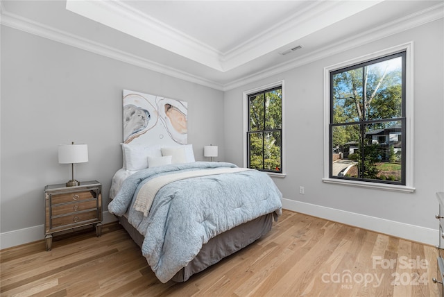 bedroom with a tray ceiling, hardwood / wood-style floors, and ornamental molding